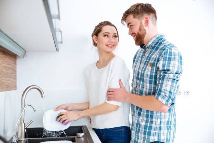 Beautiful woman washing dishes on the kitchen and handsome man wants to help her