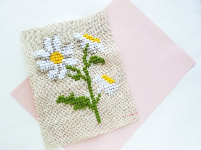 Easy Cross Stitch Pattern - three white and yellow daisies, with off-white shading, with green stem and leaves on burlap fabric