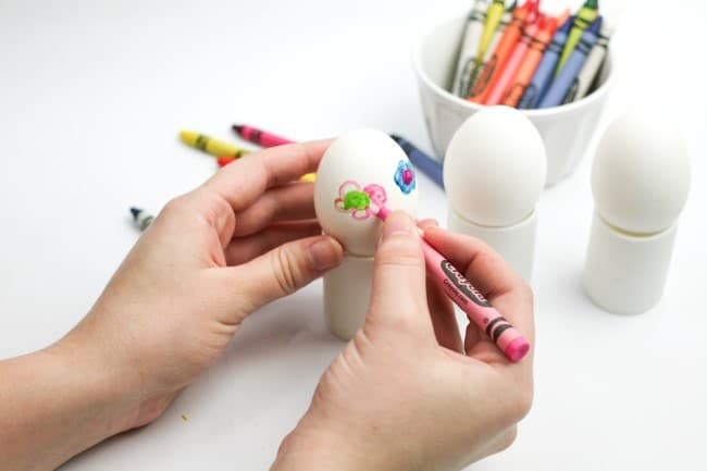 Easter egg craft - child's hands coloring egg with pink crayon