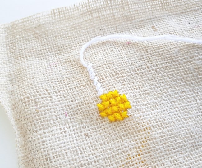 Easy Cross Stitch Pattern - white yarn stitching above the yellow on the burlap fabric.