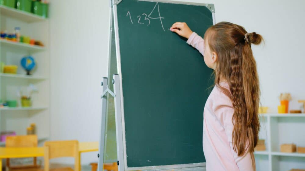 girl writing numbers on chalkboard