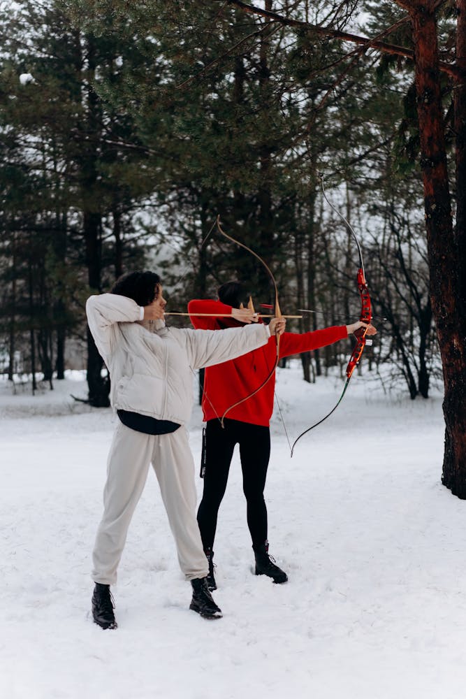 Two people practicing archery in a snowy forest setting, focused on their targets.