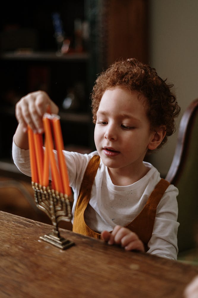 Young boy with curly hair lighting menorah candles, celebrating Hanukkah at home.
